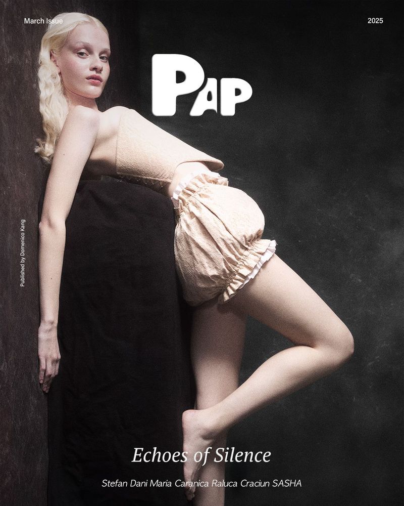 Magazine cover featuring a slender albino woman in a soft peach-colored romper, leaning against a dark background and black object.