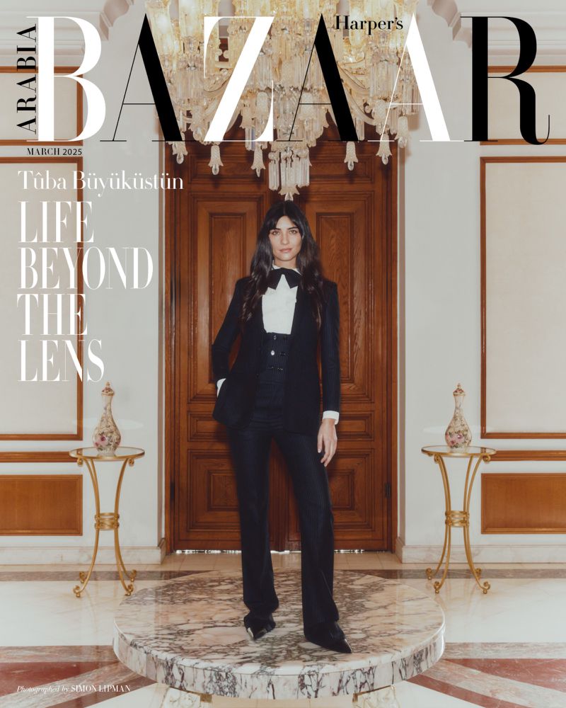 Magazine cover featuring a woman in a black suit standing on a marble platform in front of a wooden door and chandelier.