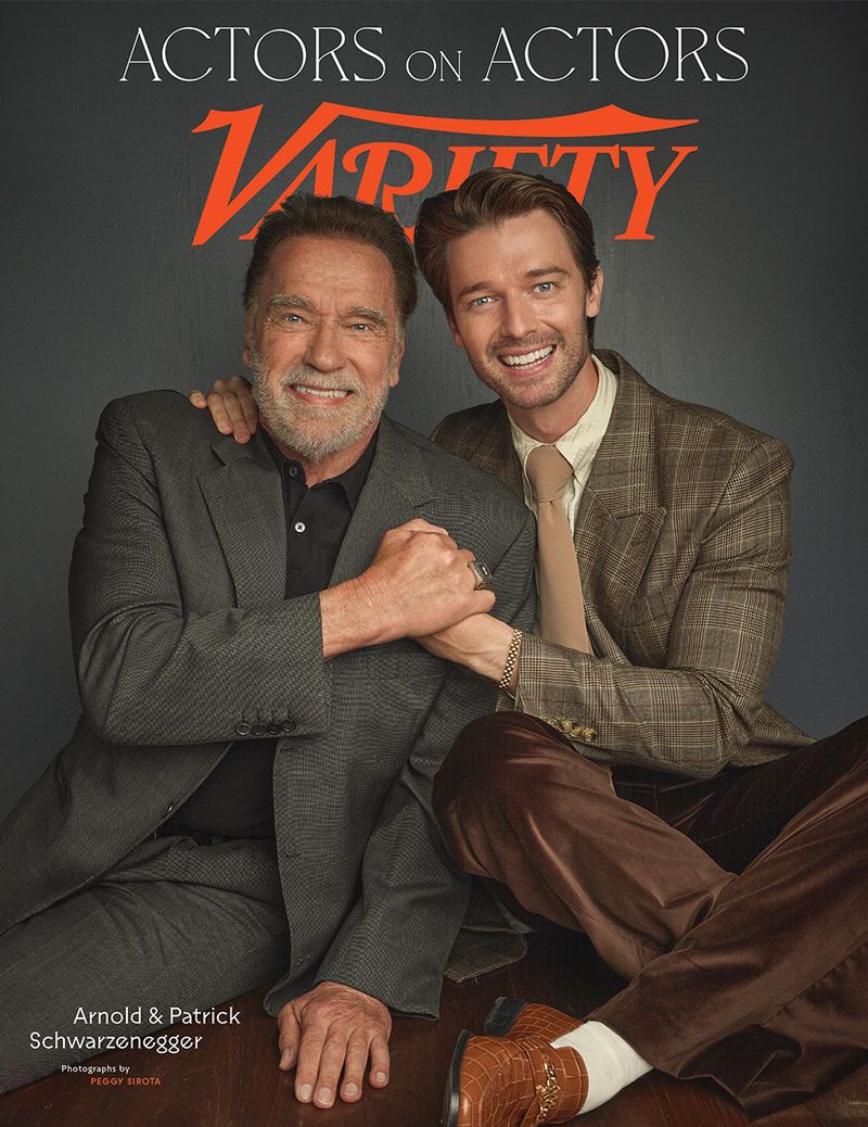Arnold Schwarzenegger and Patrick Schwarzenegger pose for Variety's Actors on Actors, in a medium shot with a gray background.