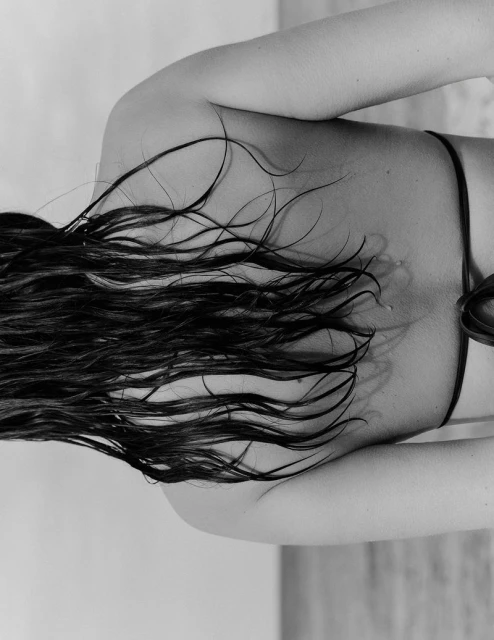 Close-up shot of the back and shoulders of an adult female with long wet hair, wearing a bikini top, in black and white.