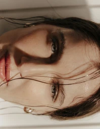 Close-up portrait of model Laetitia Casta with wet dark hair across her face for Madame Figaro