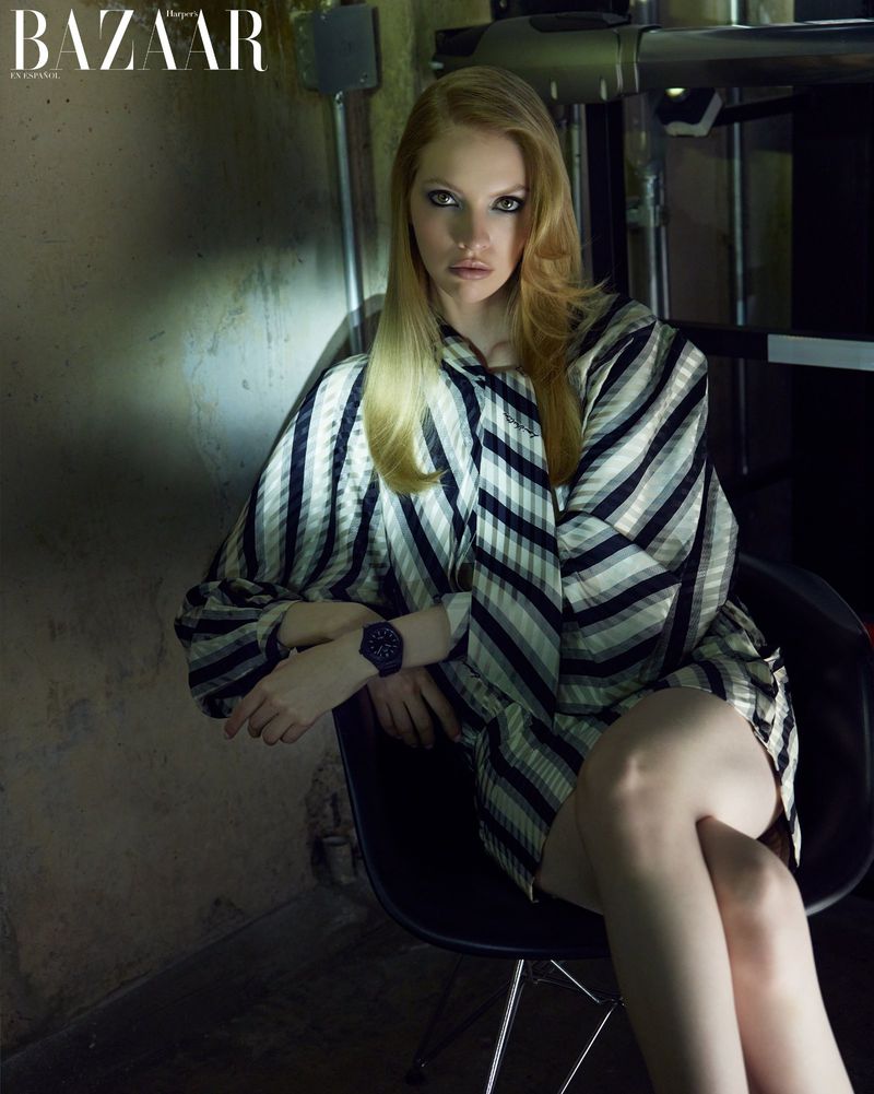 Elegant woman in a striped blouse posing on a chair in a studio setting, illuminated by studio lights and shot at eye level.