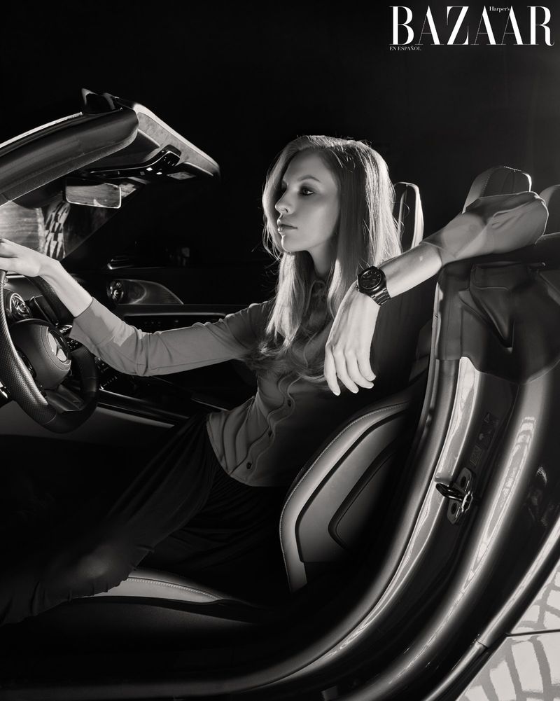 Black and white portrait of a blonde female model in a convertible car wearing a watch, with the Bazaar magazine logo visible.