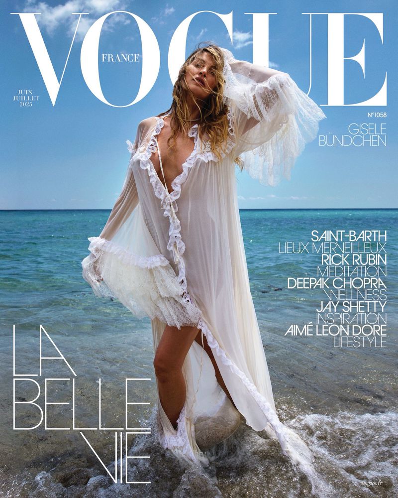 Vogue France cover featuring Gisele Bündchen in a sheer white dress, standing on a beach with blue sky and ocean backdrop, magazine text visible.
