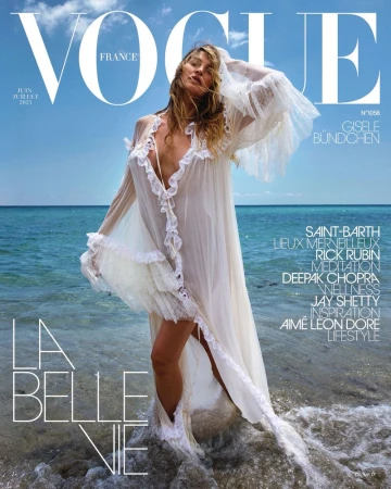 Vogue France cover featuring Gisele Bündchen in a sheer white dress, standing on a beach with blue sky and ocean backdrop, magazine text visible.