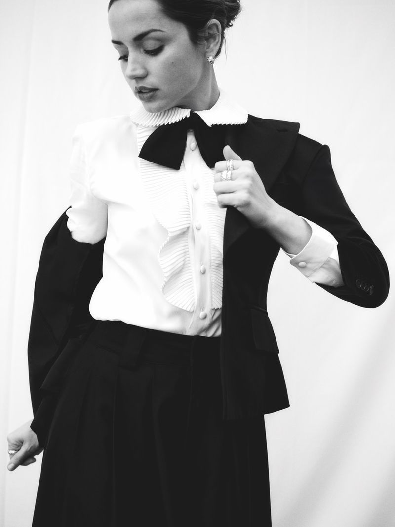 Monochrome portrait of a fair-skinned adult female model in a white collared blouse, black skirt, and jacket draped over one shoulder.