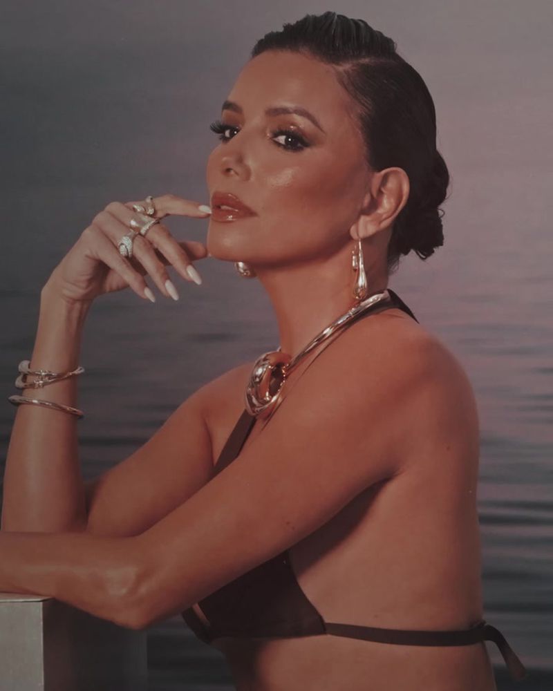 Attractive adult female in a bikini and jewelry posing in a photo studio with a water-like backdrop and soft, diffused lighting.
