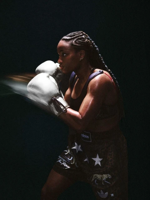 Female boxer in motion wearing sports bra and patterned shorts with boxing gloves, set against a dark background, highlighting her athleticism.