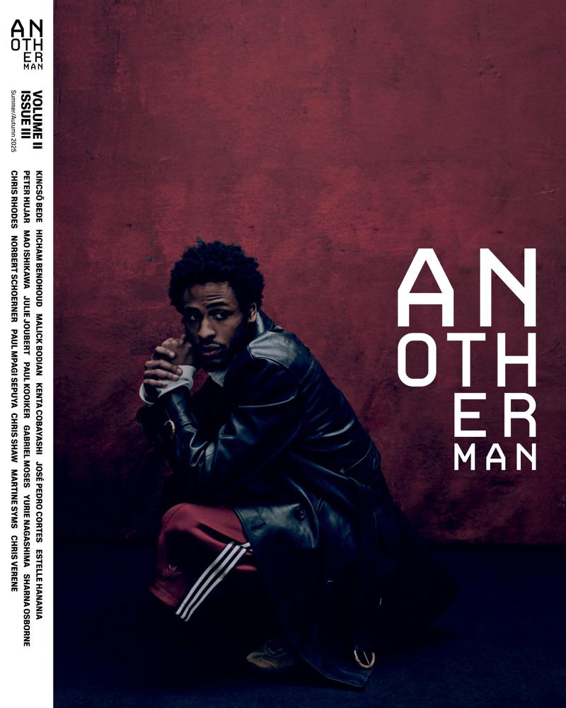 Magazine cover featuring a man in a dark coat crouching in front of a textured dark red wall with large white magazine title text.