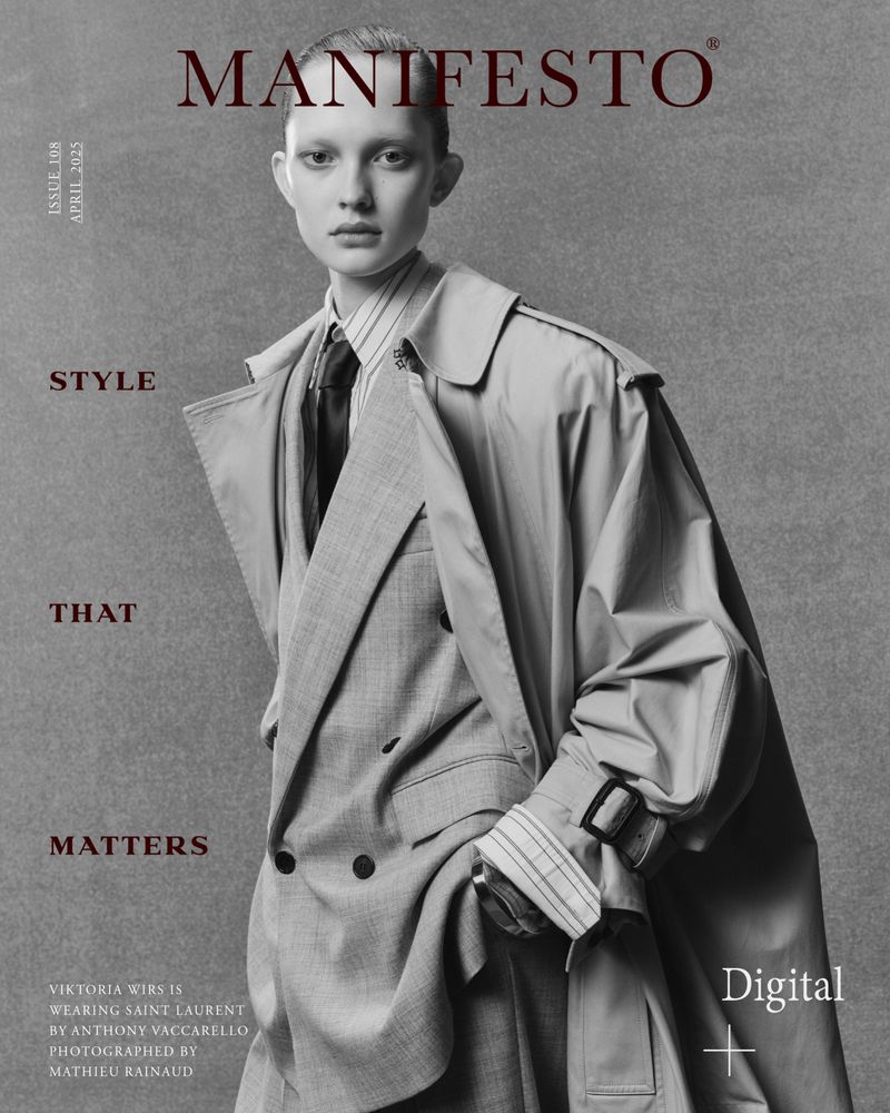 Editorial fashion portrait of a fair-skinned young woman with a grey suit and tan trench coat, styled for a magazine cover, in studio lighting.