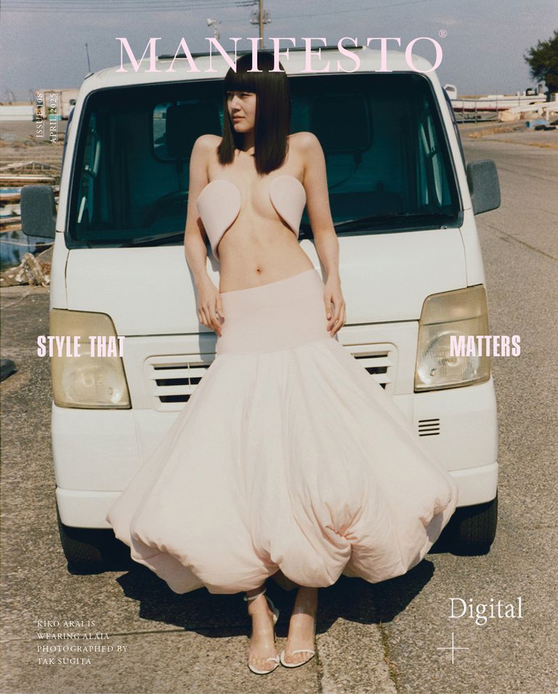 Fashion editorial shot of a woman in avant-garde pink dress posing in front of a white truck on an outdoor lot with magazine text.
