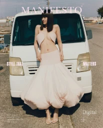 Model leaning against a white van wearing a strapless pale top and voluminous skirt