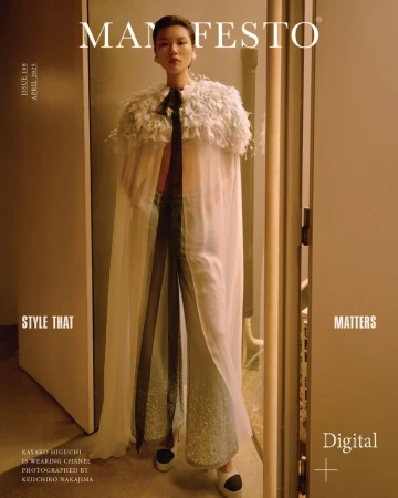 Kayako Higuchi wearing a sheer white feathered cape and embellished wide-leg trousers standing in an open doorway.