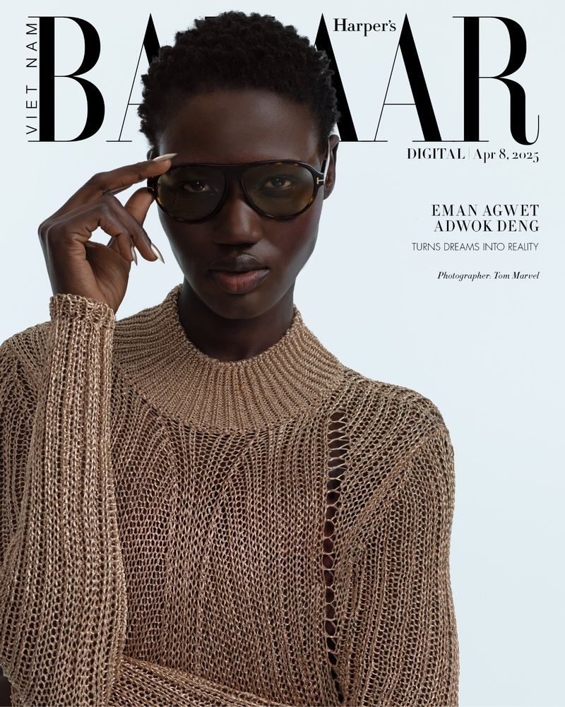 Model Eman Deng wearing dark aviator sunglasses and a textured brown knit sweater against a light studio backdrop.