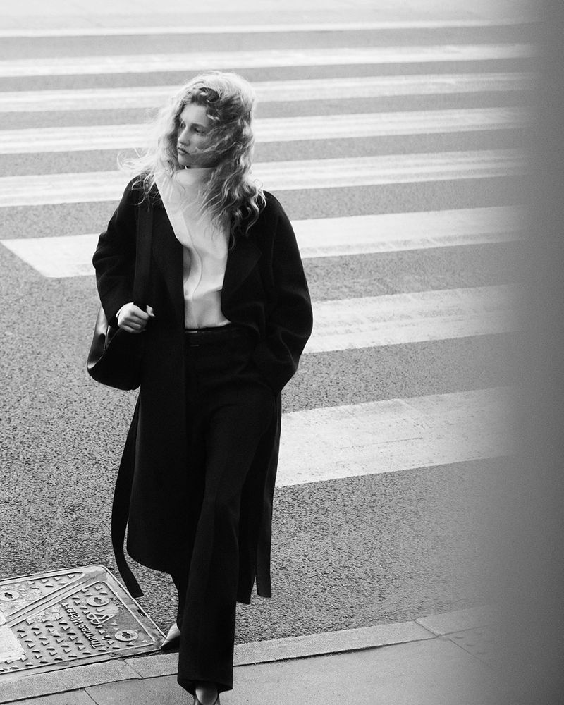 Model Apolline Rocco Fohrer walking outdoors in a black coat for COS Outerwear 2024