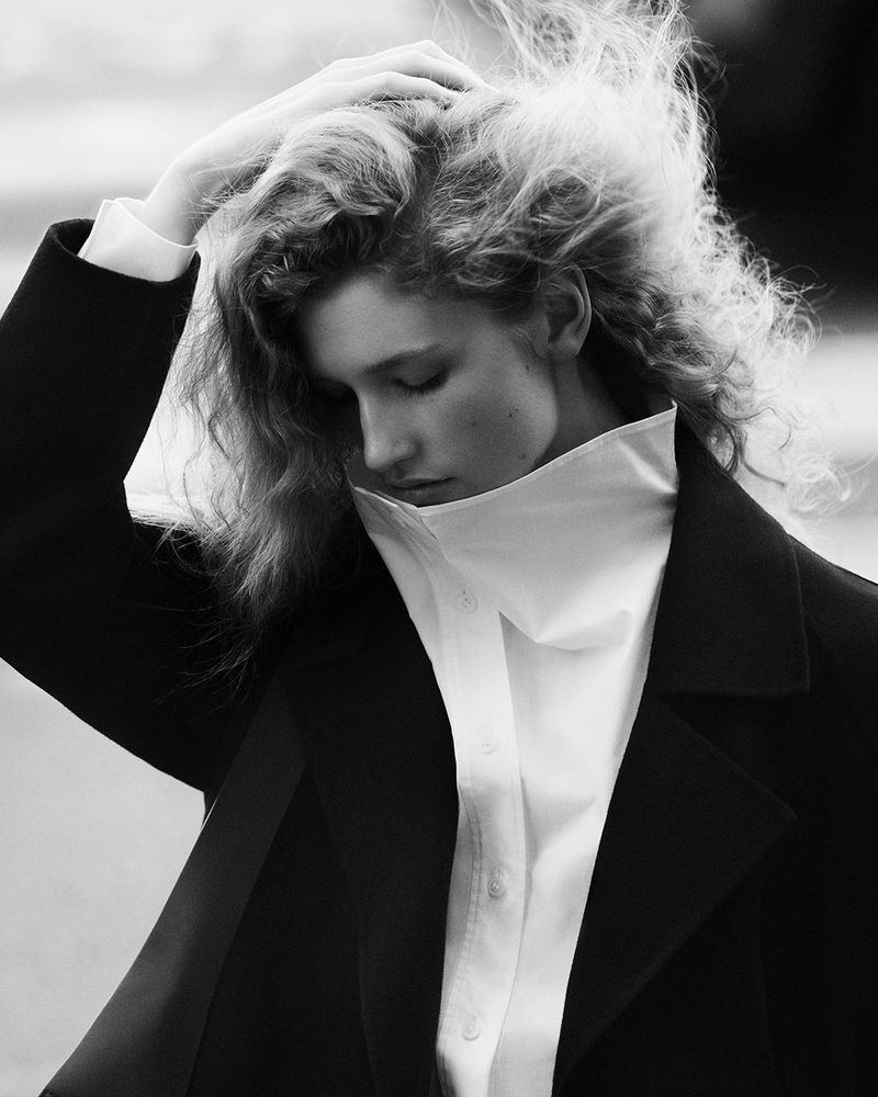 Model with tousled hair wearing a black coat and high-collared white shirt