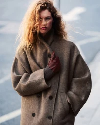 Model with long curly hair wearing a brown wool coat and leather gloves outdoors