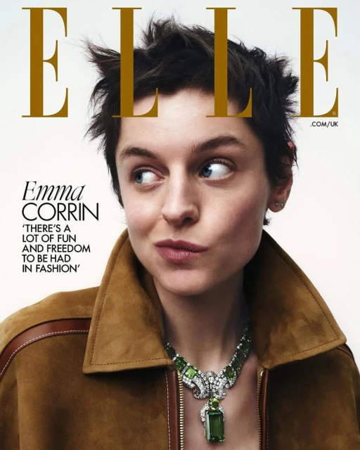 Emma Corrin on Elle Magazine cover in a brown jacket and large green necklace. The image features a clean studio backdrop.