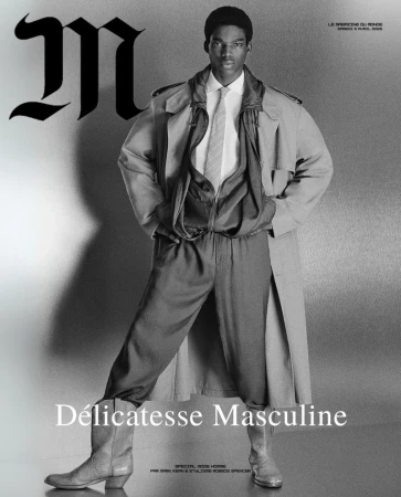 Black male fashion model in trench coat, shirt, tie, and boots poses for a black and white studio shot, showcasing masculine elegance.