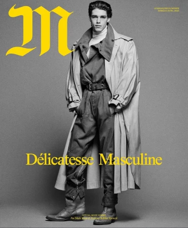 Magazine cover featuring a young male model in a stylish trench coat, dark jumpsuit, and leather boots against a grey backdrop.