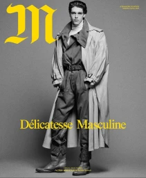 Model wearing a layered coat and jumpsuit over boots against a grey studio backdrop for M Le magazine du Monde.