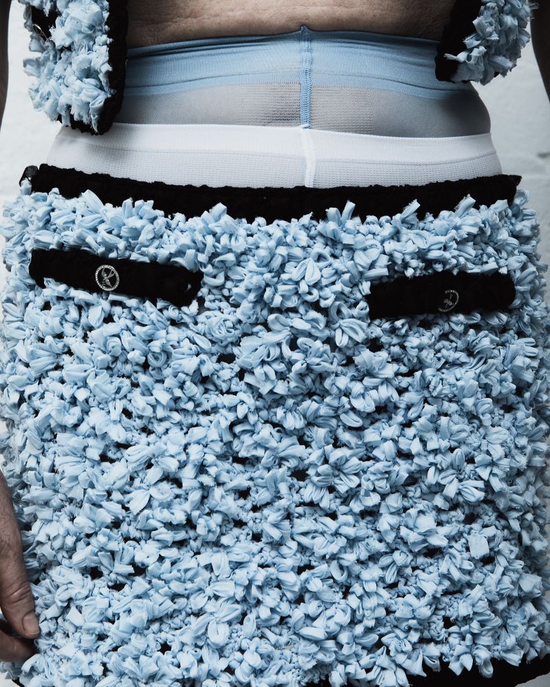 Close-up of a person wearing a light blue mini skirt and matching vest with a black trim, accessorized with sheer blue leggings.