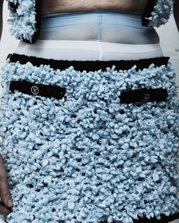 Close-up of a person wearing a light blue mini skirt and matching vest with a black trim, accessorized with sheer blue leggings.