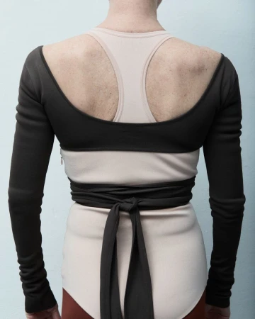 Back view of a person wearing a black wraparound top, beige top, and briefs. The model is positioned against a light blue backdrop.