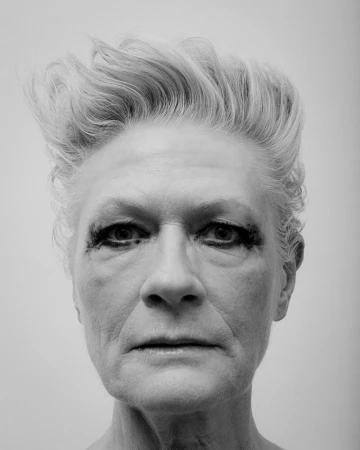 Black and white portrait of an elderly woman with short, styled hair and heavy eye makeup looking directly at the camera.