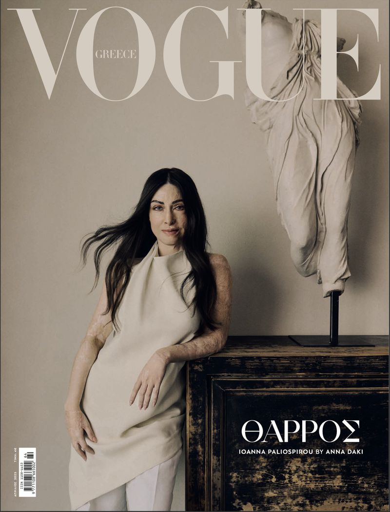 Vogue Greece magazine cover featuring a brunette woman in a cream dress leaning against an antique wooden table with a statue.
