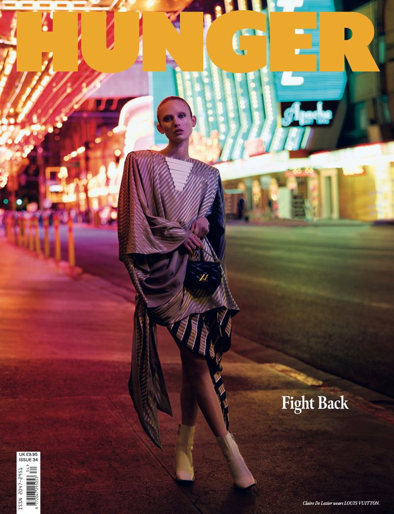 Fashion magazine cover featuring a female model in a unique dress, set against a brightly lit urban backdrop, 'Hunger' magazine.