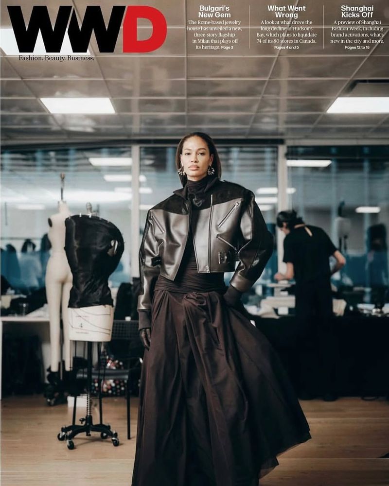 Fashion editorial showcasing a model in a cropped leather jacket and long dress, posing indoors with a sewing mannequin in the background.