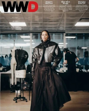 Joan Smalls wearing a cropped black leather jacket and flowing black skirt inside a design atelier for the WWD magazine cover.