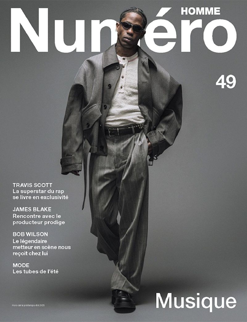 Travis Scott poses on the cover of Numero Homme 49, wearing a grey suit and sunglasses against a grey backdrop with magazine text.