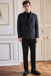 Model wearing a dark grey double-breasted suit standing in an apartment with panelled doors and parquet flooring.