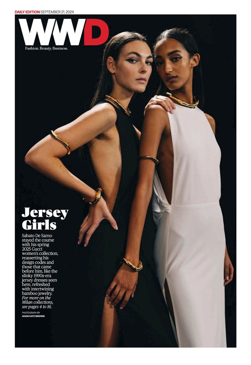 WWD magazine cover featuring two fashion models wearing black and white dresses, accented with golden arm and neck bands on a dark backdrop.
