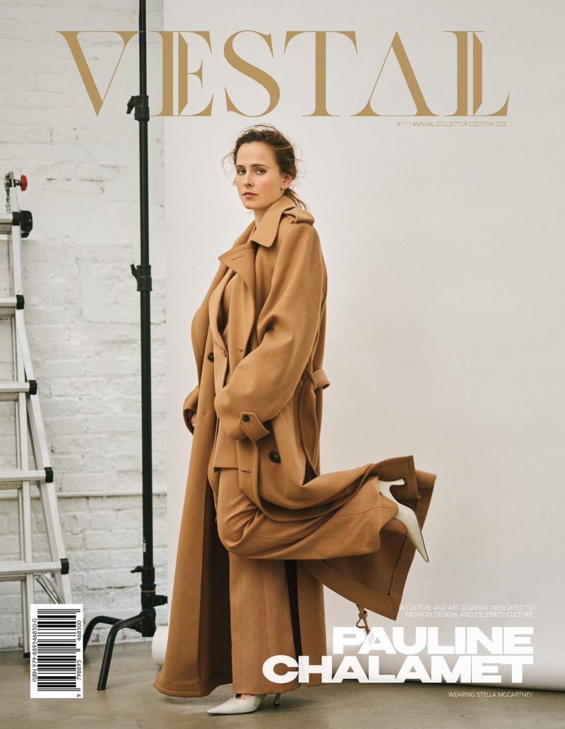 Magazine cover featuring a model in a tan coat and pants, posing in a photo studio with ladder and lighting equipment.