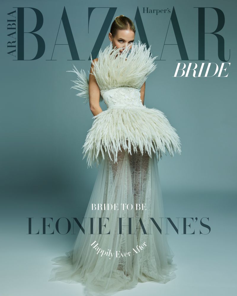 Fashion editorial cover featuring a blonde woman in a feathered wedding dress, with BAZAAR BRIDE masthead, against a grey background.