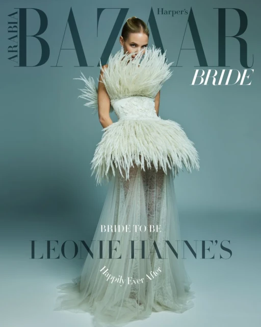 Fashion editorial cover featuring a blonde woman in a feathered wedding dress, with BAZAAR BRIDE masthead, against a grey background.