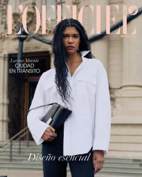 Model wearing a white button-down shirt and black trousers holding a black handbag in front of a classic building exterior.
