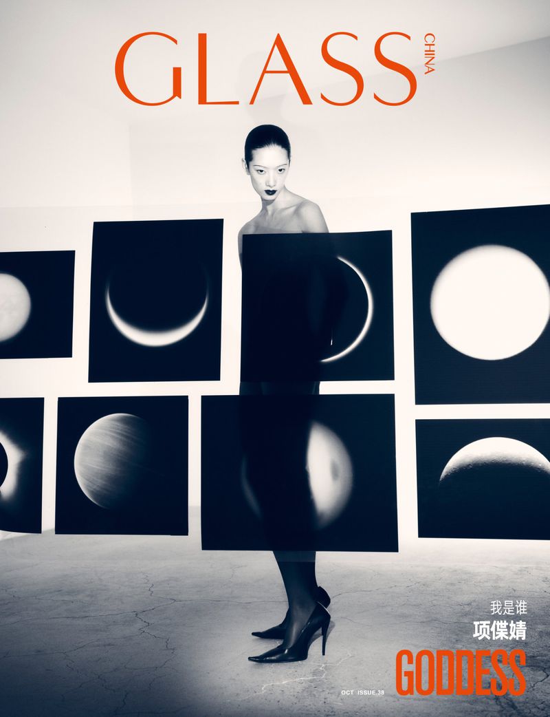 Fashion editorial cover shot features an Asian model in an elegant black dress, posing in front of arranged prints in a minimalist studio.