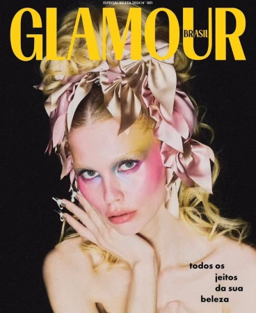 Model with blonde hair, pastel eyeshadow, and satin bows in her hair posing against a black background for a magazine cover