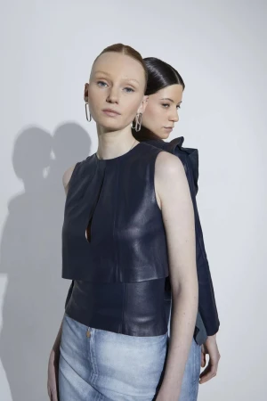 Two female models posing back to back wearing leather tops against a white studio wall