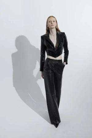 Model wearing a black leather cropped jacket and matching trousers standing against a white seamless background