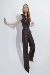 Model wearing a dark leather sleeveless top and matching trousers posing against a bright white seamless background