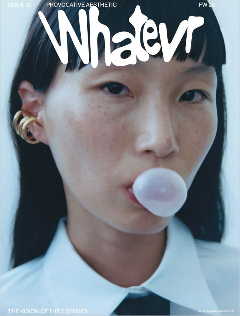 Close-up of a young woman with an expressive face blowing a bubble in front of a fashion magazine cover with bold typography.