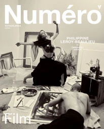 Monochrome magazine cover featuring a woman posing dynamically in an art studio with a seated artist working on a canvas.