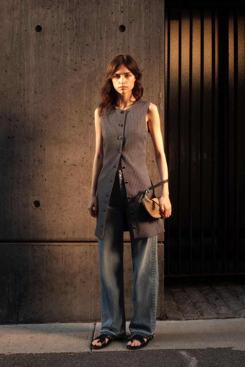 Model Ana Rossolovich wearing a patterned sleeveless tunic and denim jeans standing outdoors in a city setting.