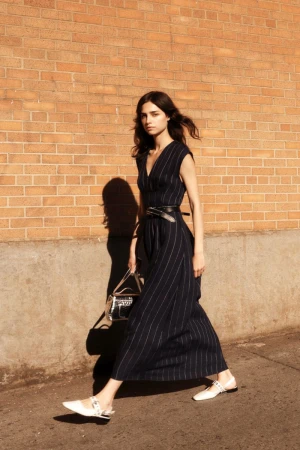 Model in dark pinstripe dress walking along a concrete wall with a brick background