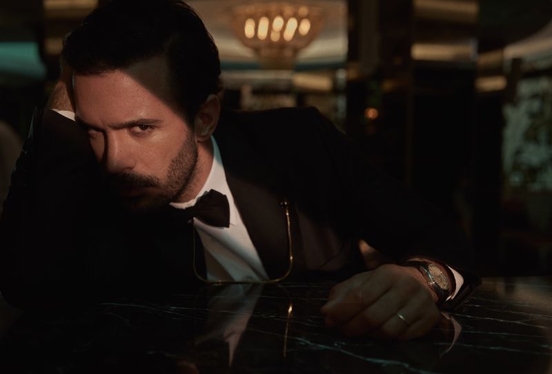 Man in suit and bow tie leans on black marble bar with moody lighting, creating a sophisticated and mysterious portrait.